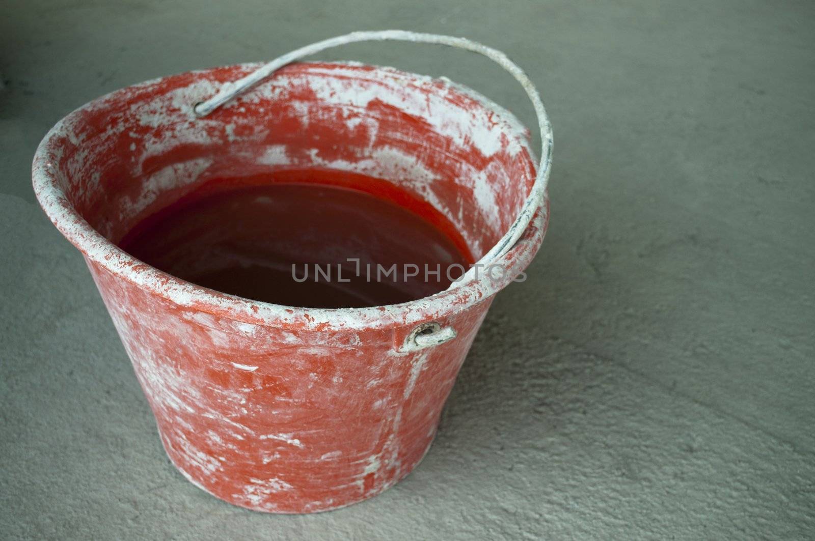 Red bricklayer bucket full of water over a gray cement floor