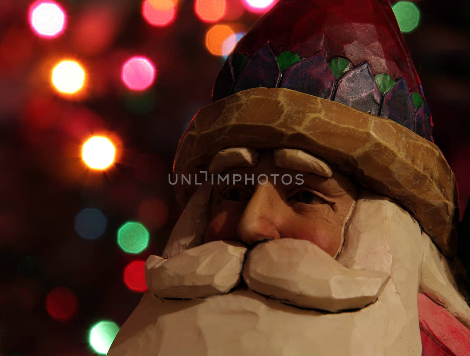 A santa claus figurine with Christmas lights in the background.
