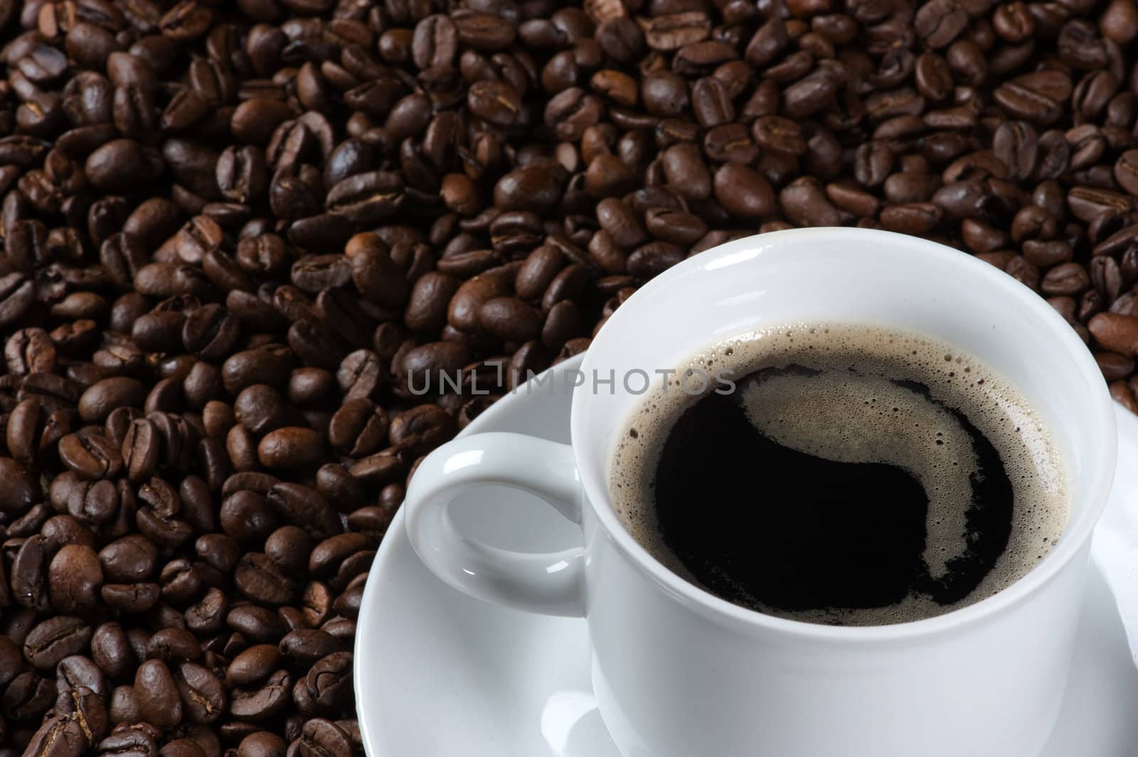 Closeup of a cup of fresh coffee, served on a plate covered with freshly roasted coffee beans