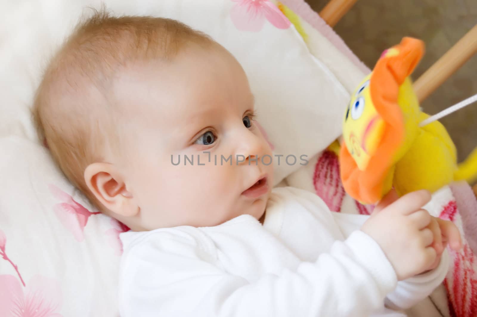 Baby lying in bed and playing with toy