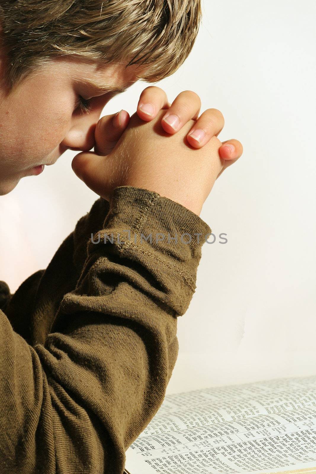 shot of a young boy praying over the bible on white