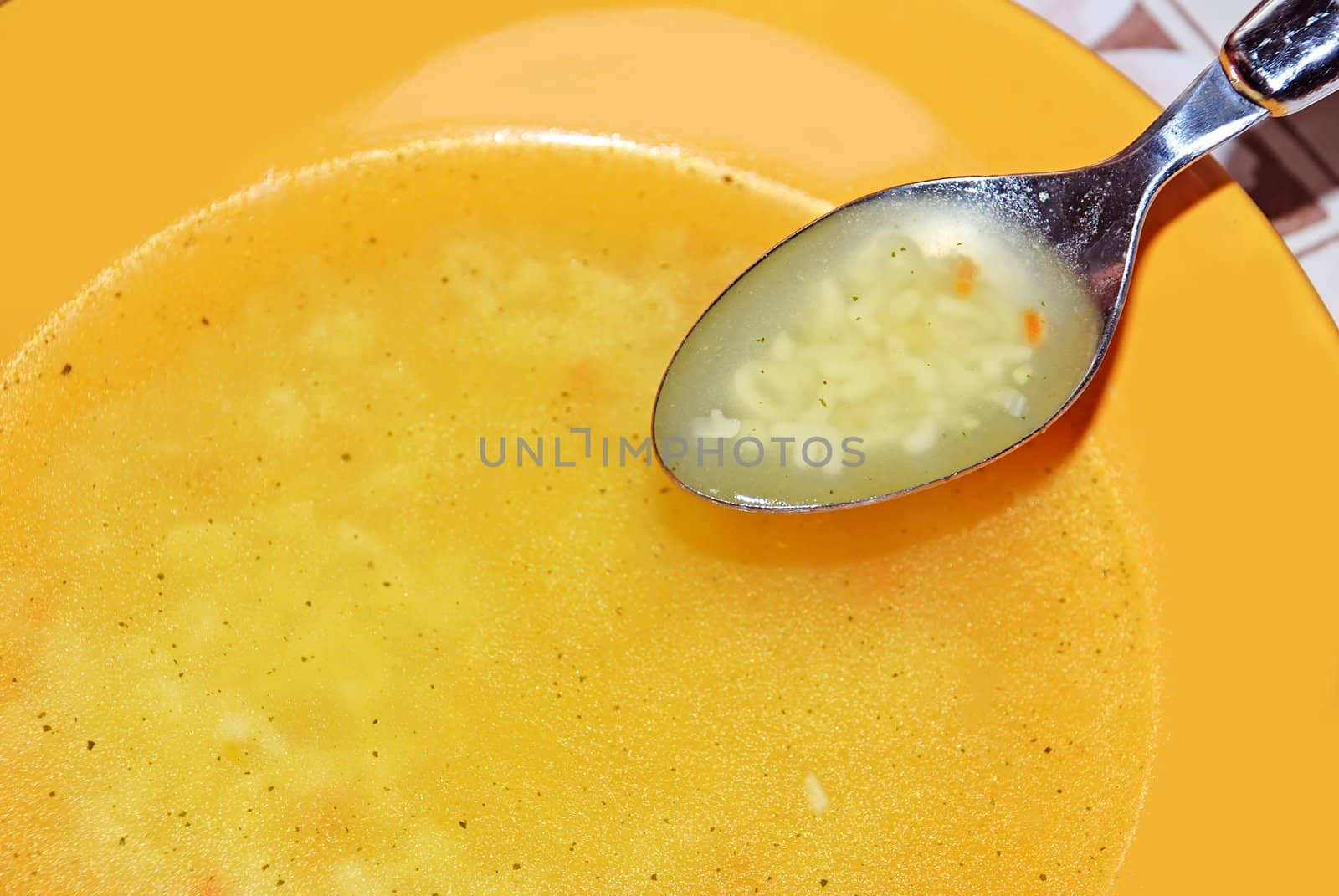 Soup in yellow plate and spoon closeup
