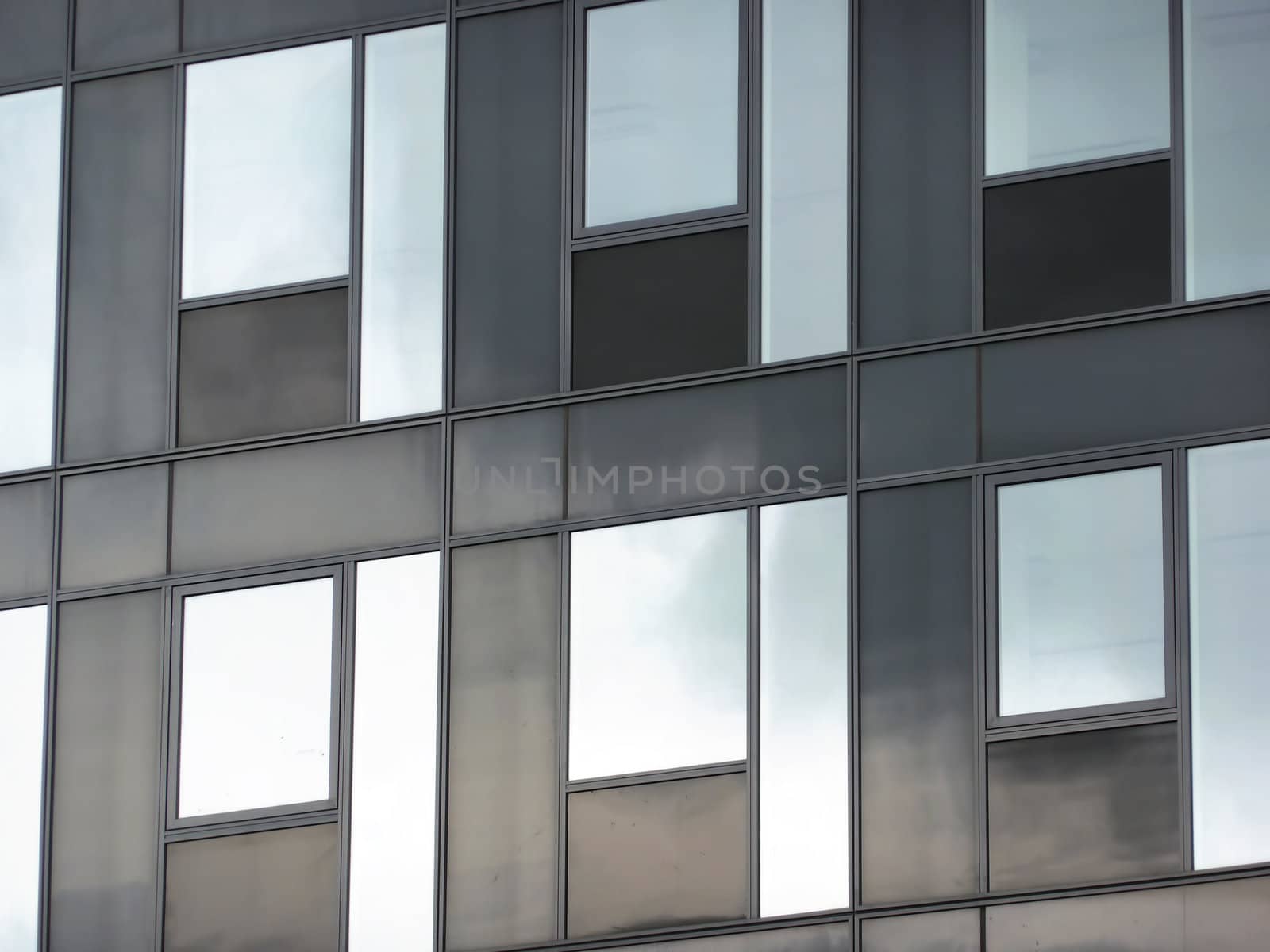 Modern black glass facade reflecting blue sky with clouds