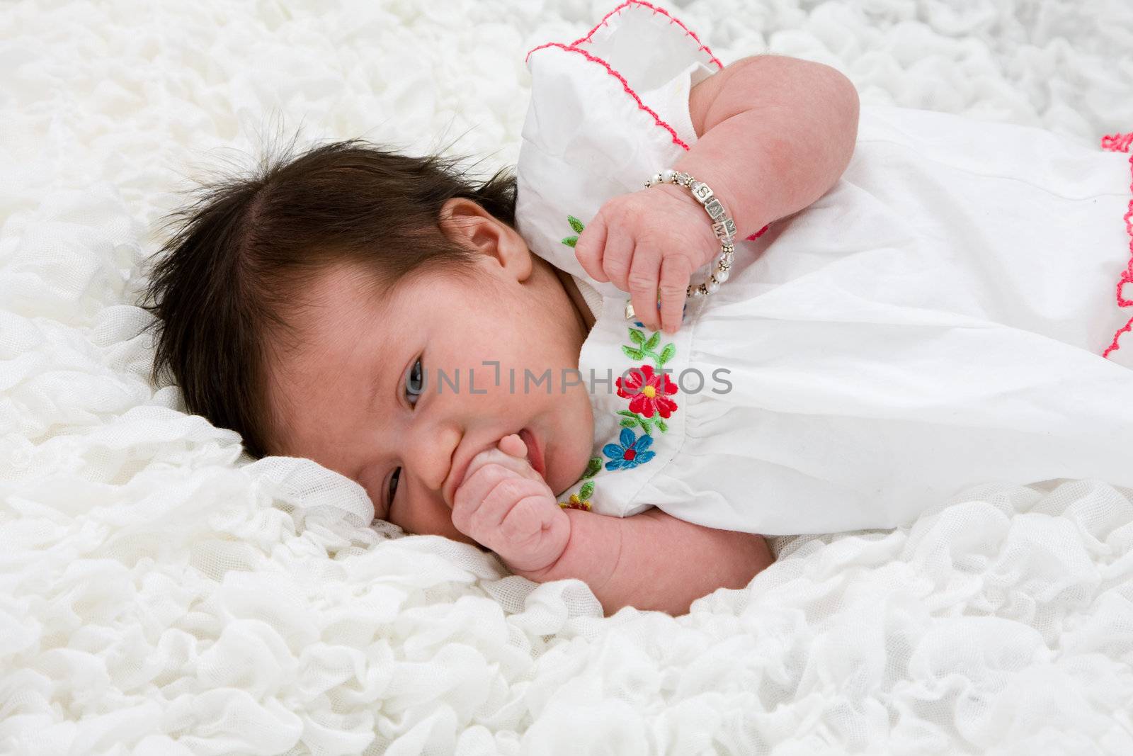 Baby with brown hair laying on white blanket