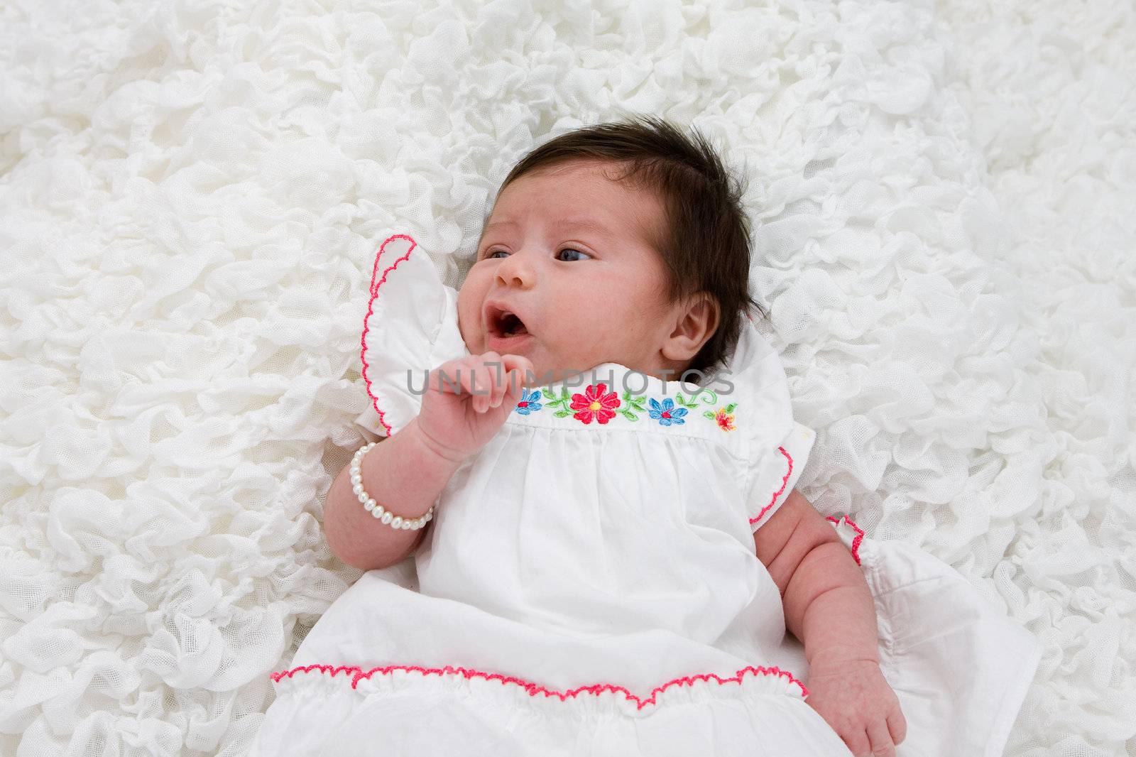 Baby with brown hair laying on white blanket