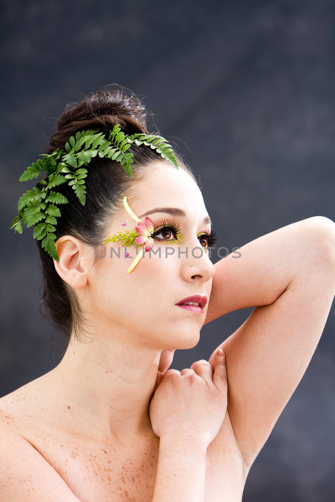 Beautiful brunette face with pink green yellow eye flower petal makeup, isolated on gray