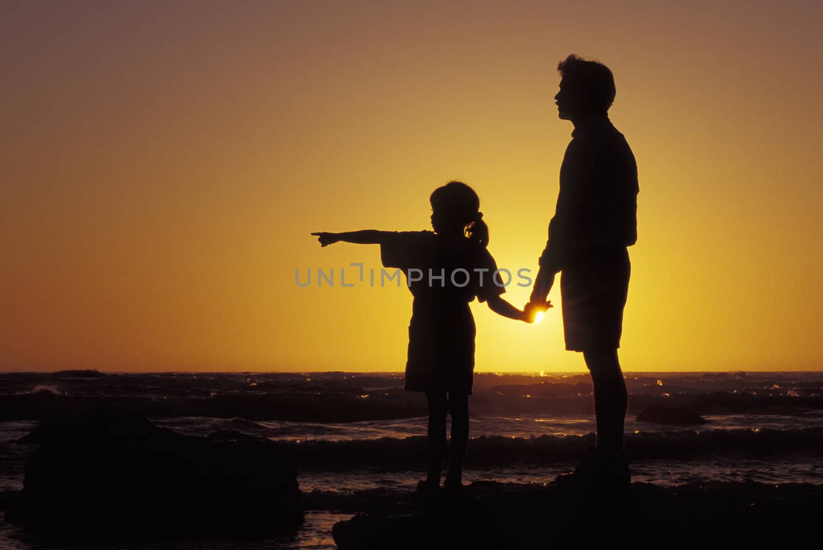 Father and daughter standing on the beach at sunset