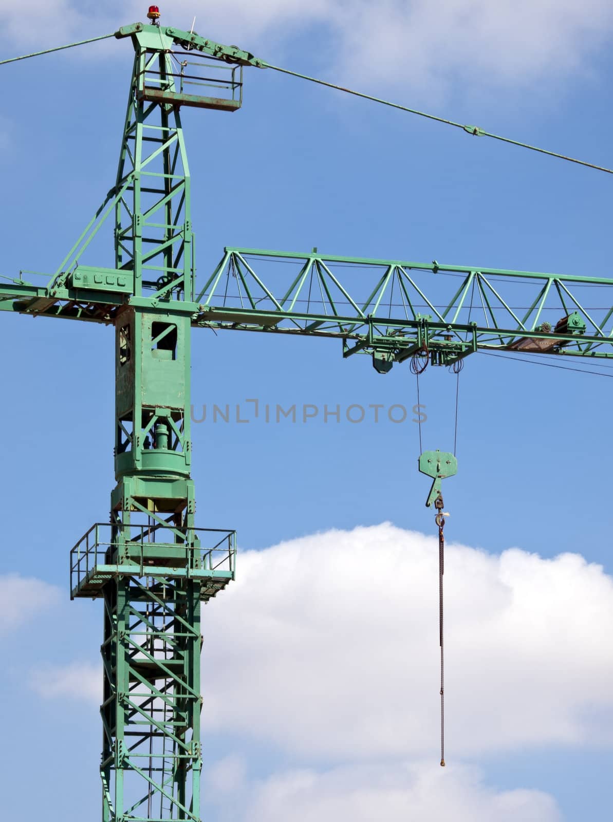 Detail of a green tower crane against a lightly clouded sky