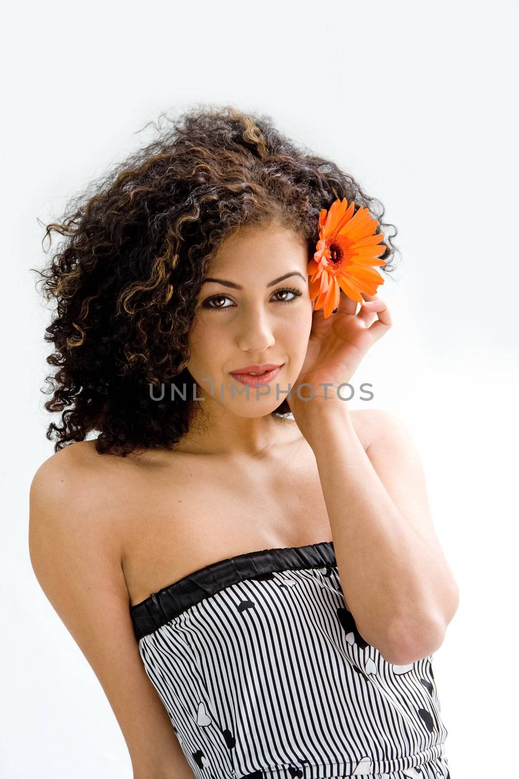 Beautiful young woman with brown curly wild hair and orange flower in hair, isolated