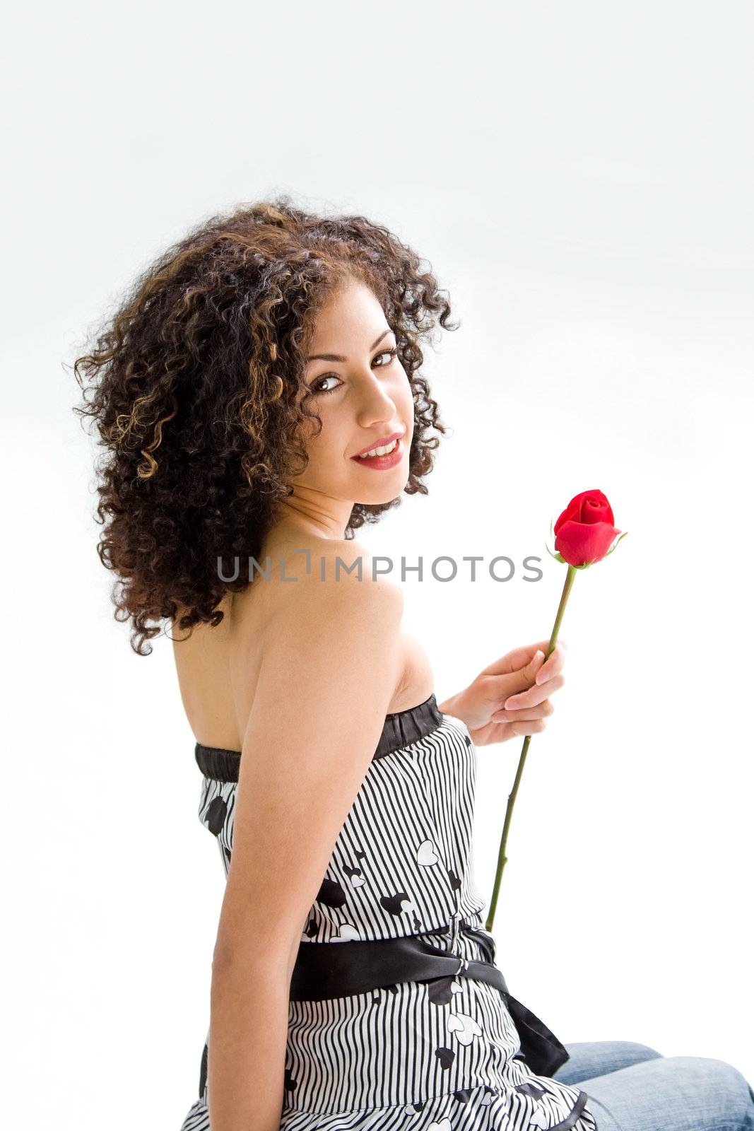 Sincere beautiful young woman with brown curly wild hair and bare shoulders holding red rose, isolated
