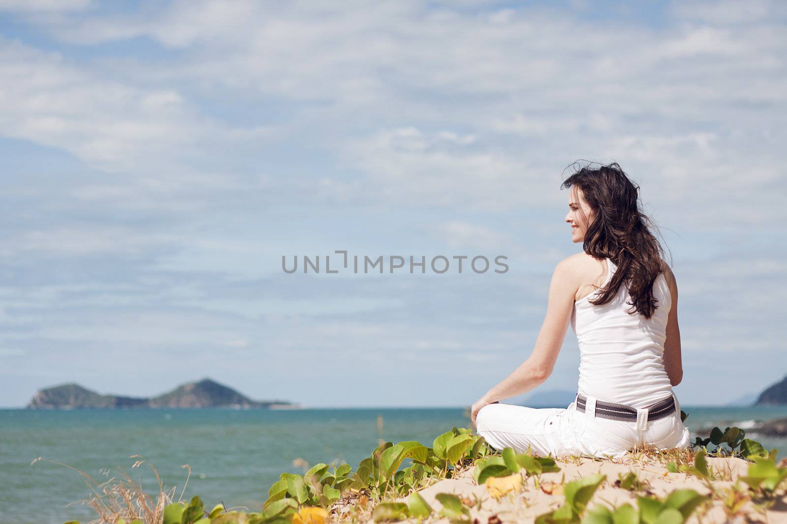An attractive woman sitting down relaxing on top of a sandune on a tropical beach 