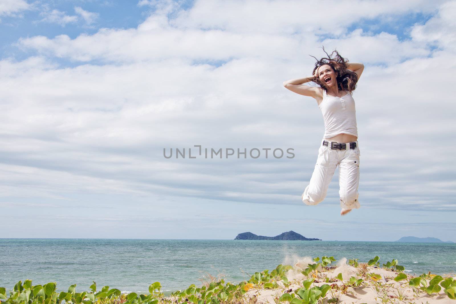 A beautiful girl jumping and laughing on a sunny tropical beach