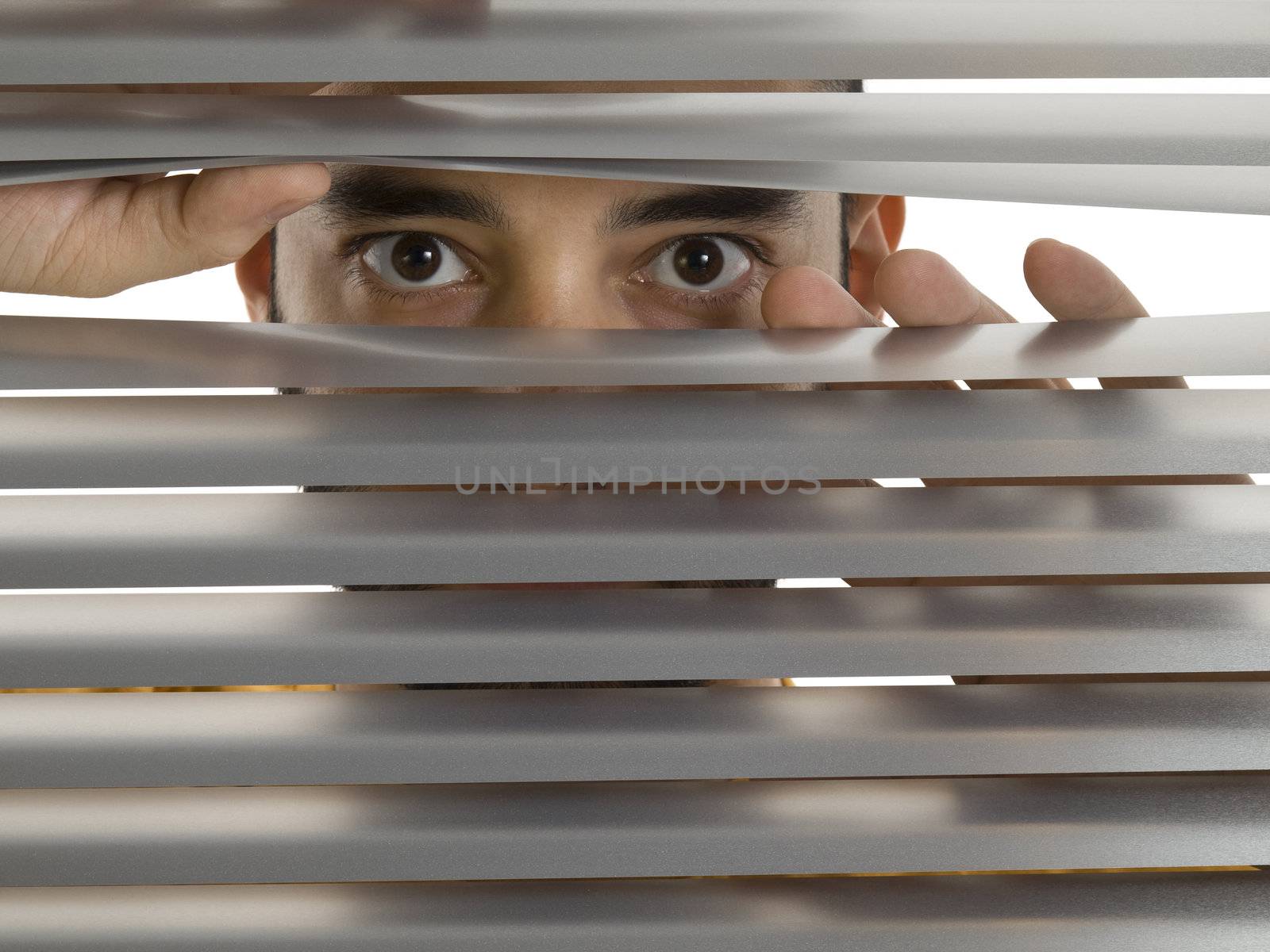 A man looks to the camera through the blinds.