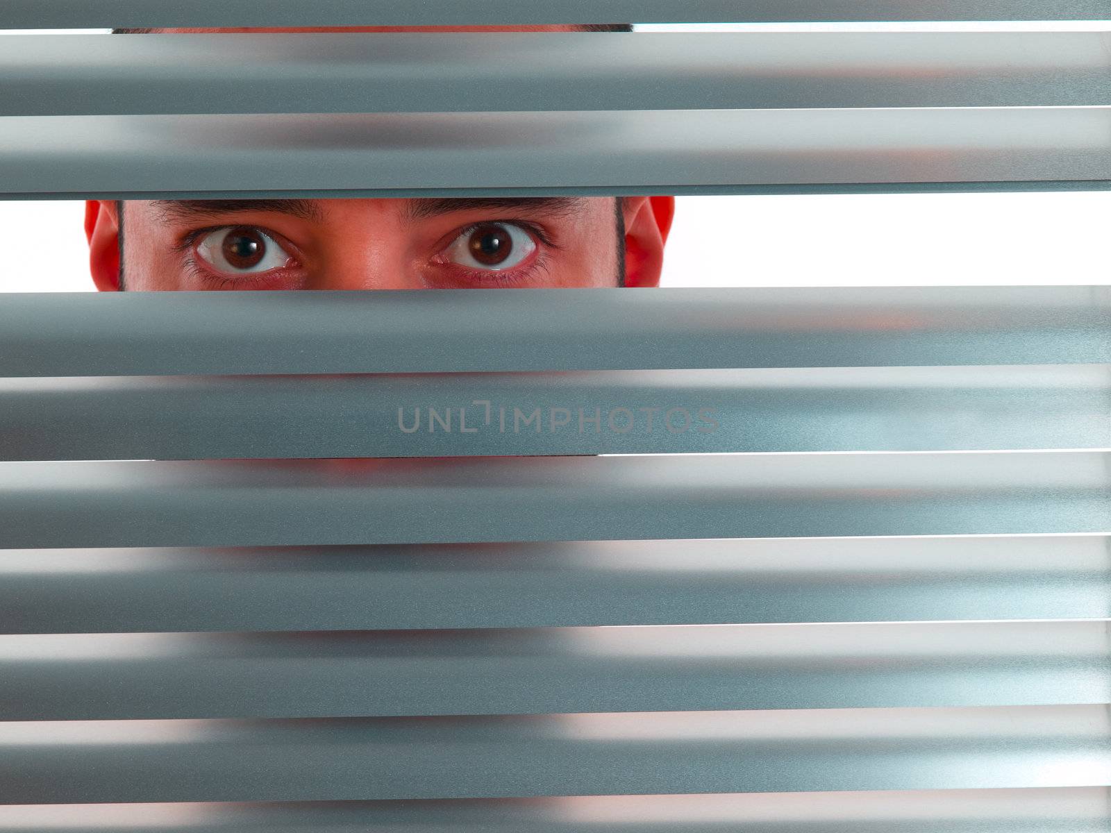 A red man looks to the camera through the blinds.