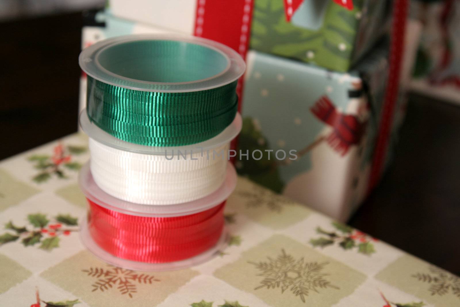 Three spools of Christmas gift wrapping ribbon sitting on already wrapped gifts.
