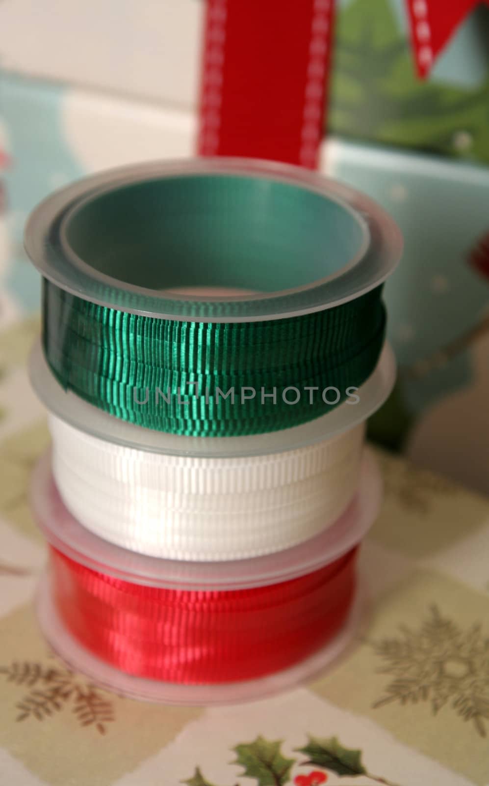 Three spools of Christmas gift wrapping ribbon sitting on already wrapped gifts.
