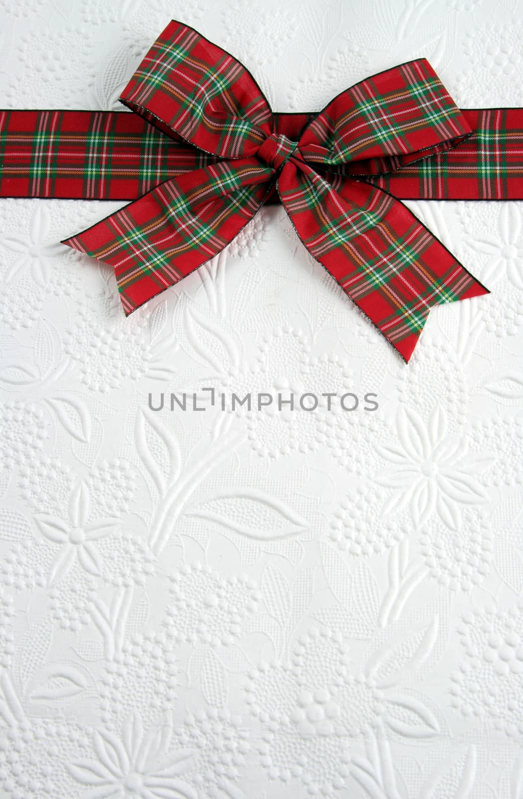 A plaid christmas bow on decorative white paper.
