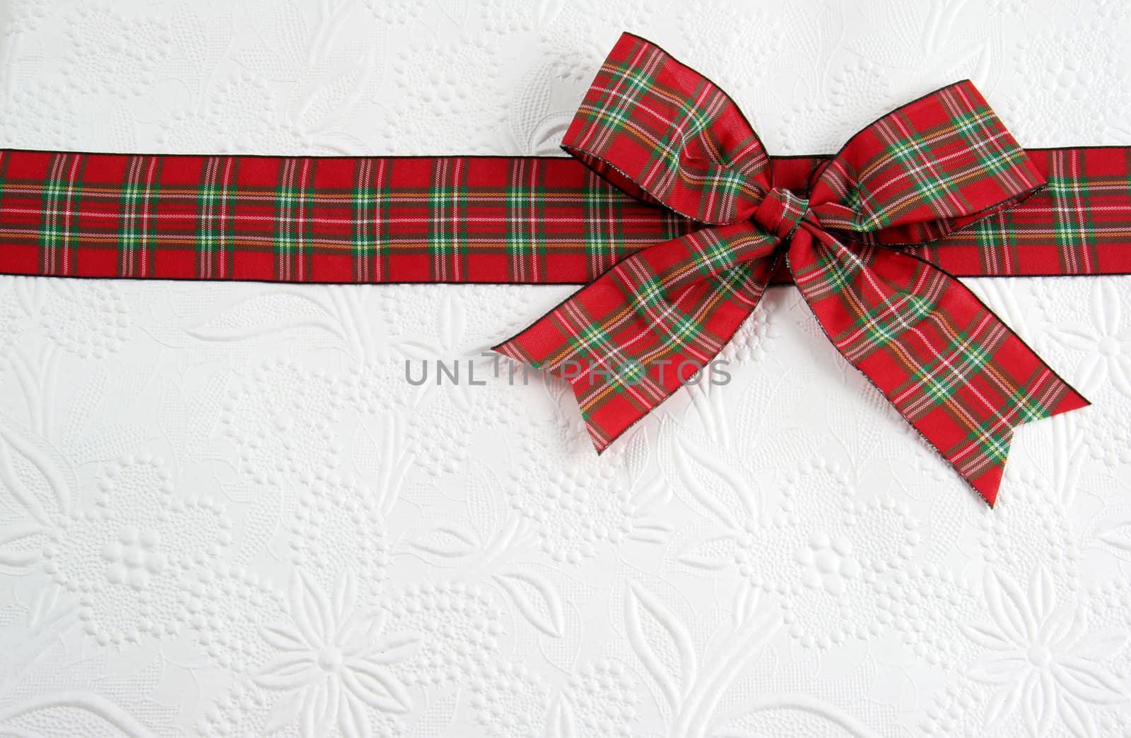 A plaid christmas bow on decorative white paper.
