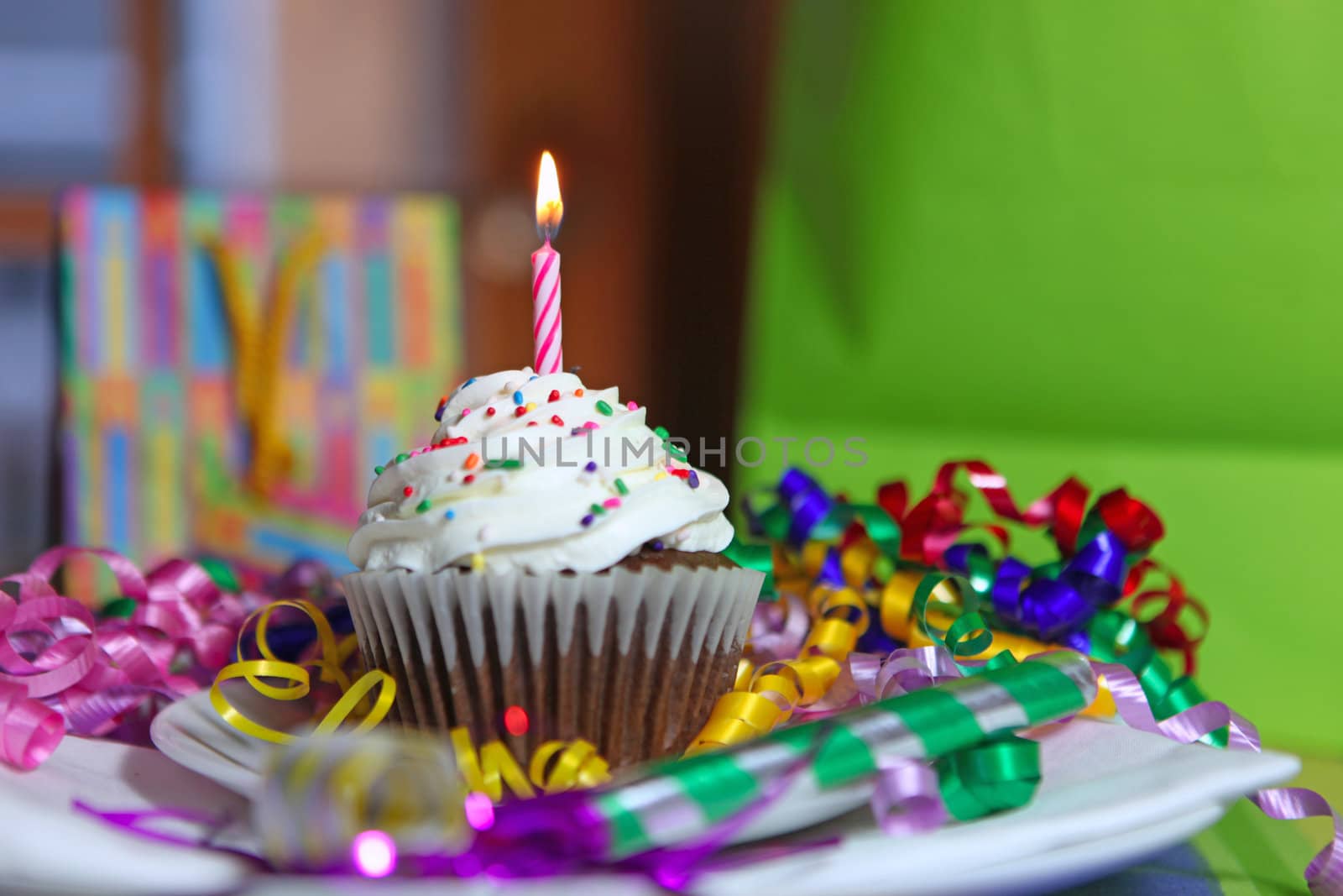 Birthday CupCake With One Lit Candle and Gifts in the Background