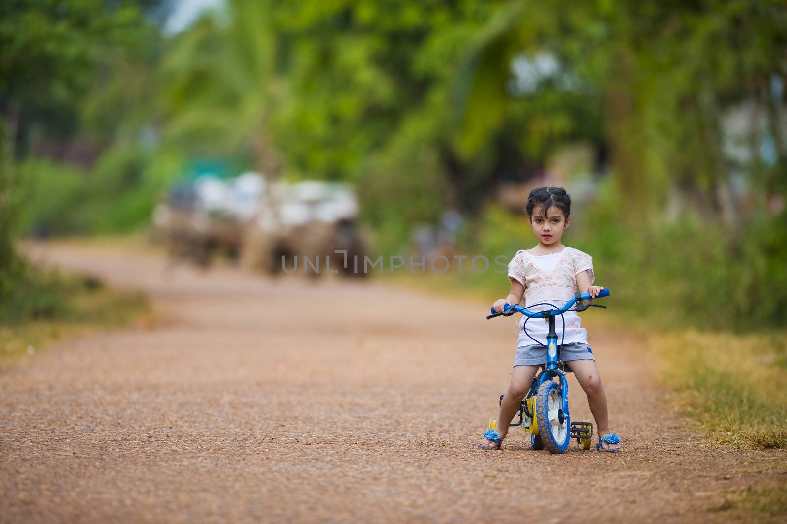 cute thai-indian girl riding her bike on a dirt road. focus on the girl with a shallow depth of field and lot of free space.