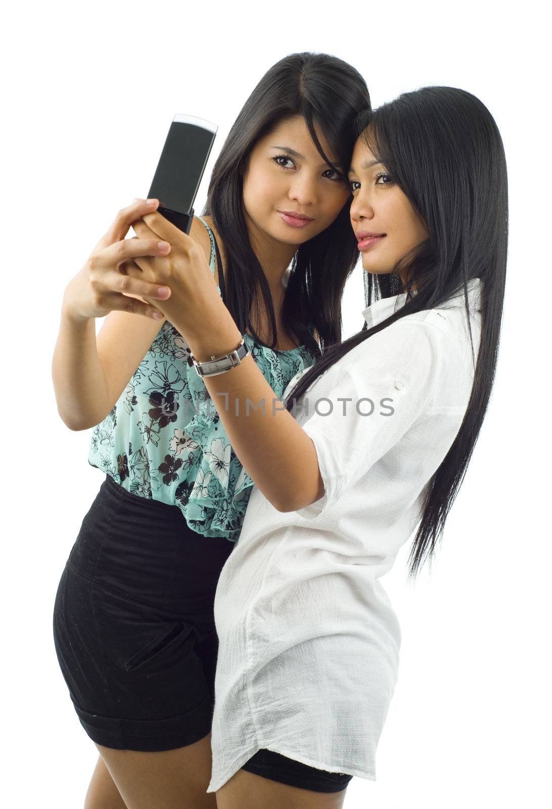 two asian women taking a picture of themselves with a mobile phone, isolated on white