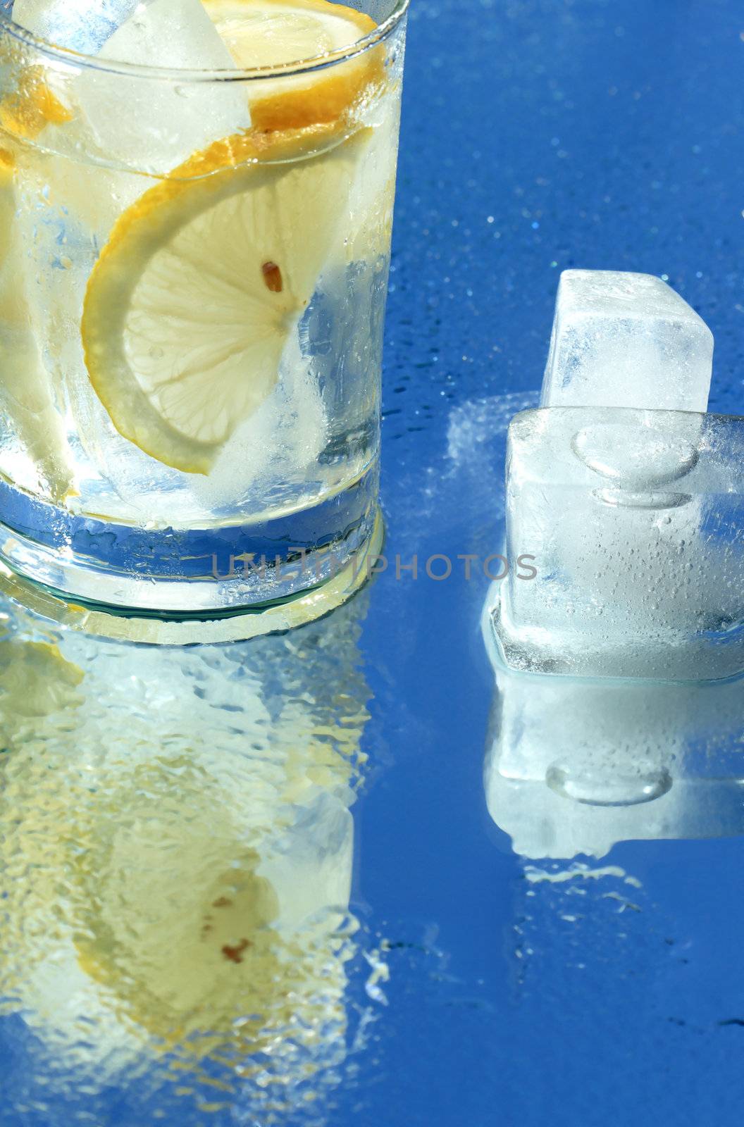 Glass of water with lemon and ice cubes on blue background