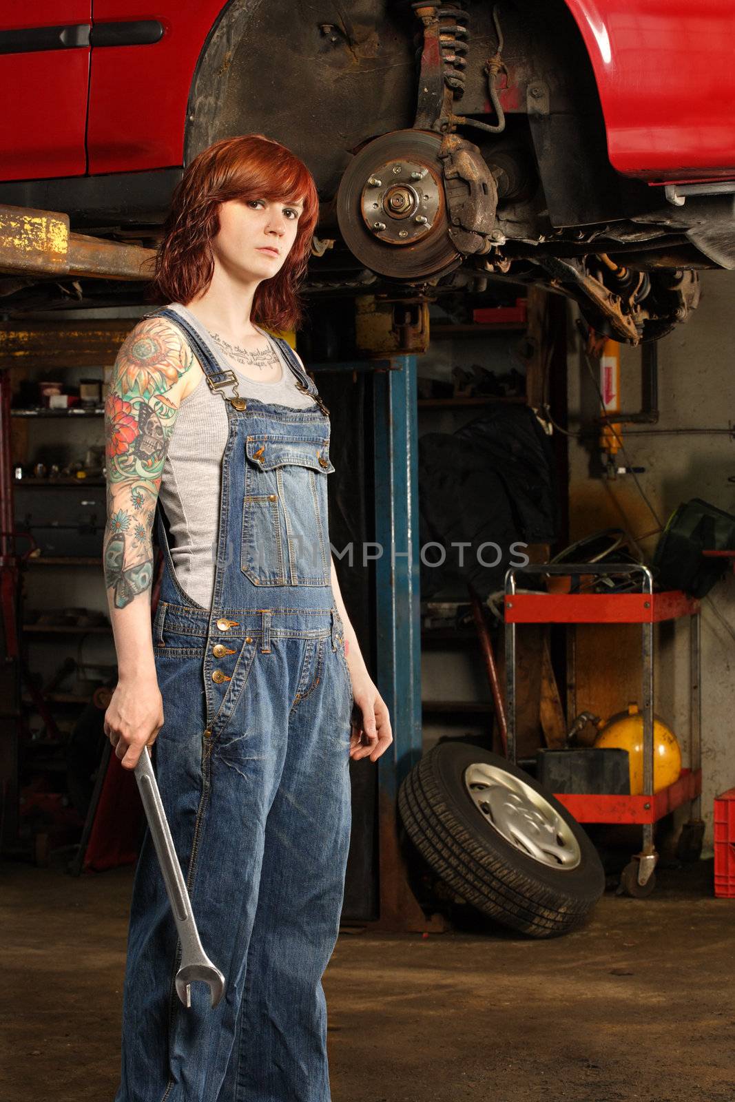 Photo of a young beautiful redhead mechanic wearing overalls and holding a huge wrench.  Attached property release is for arm tattoos.
