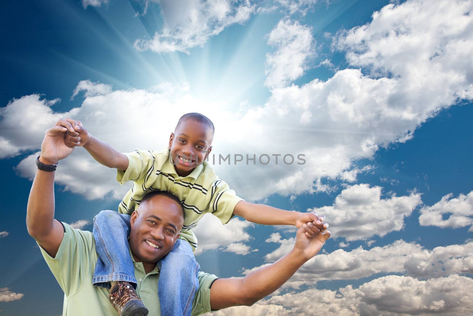 Happy African American Man with Child Over Blue Sky, Clouds and Sun Rays.