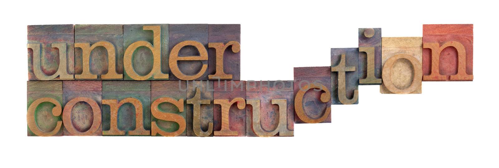 under construction words in vintage wooden letterpress type blocks, stained by color ink, isolated on white