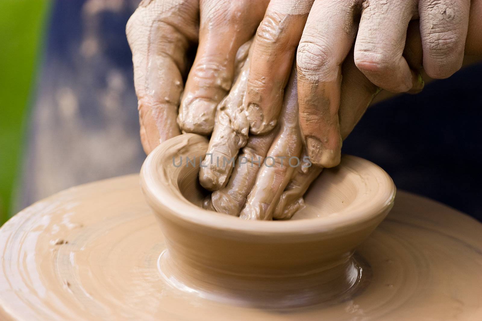 A potters hands guiding a child hands to help him to work with the ceramic wheel