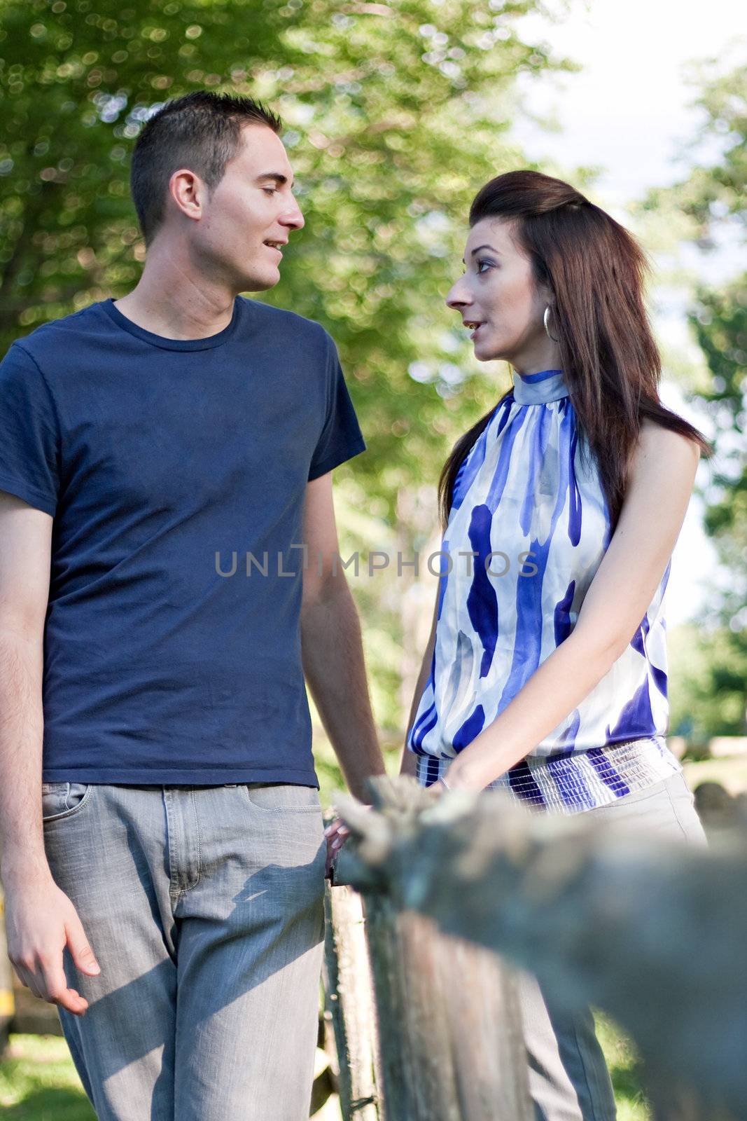 A happy young couple in their mid 20s talking to one another outdoors.