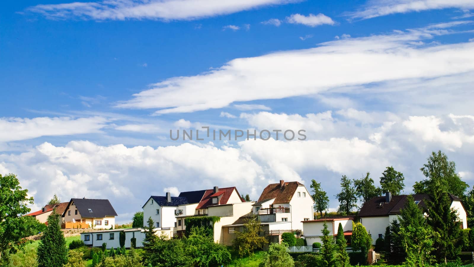Village against the summer blue sky with white clouds on a green hill