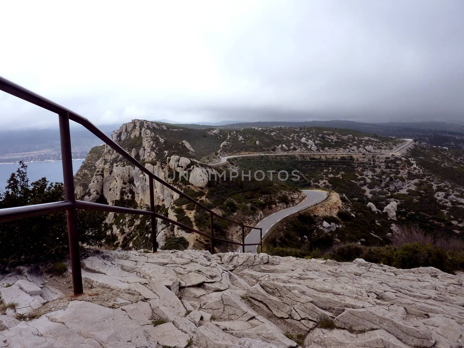 Winding road and metallic fence in a rocky mountain by cloudy weather