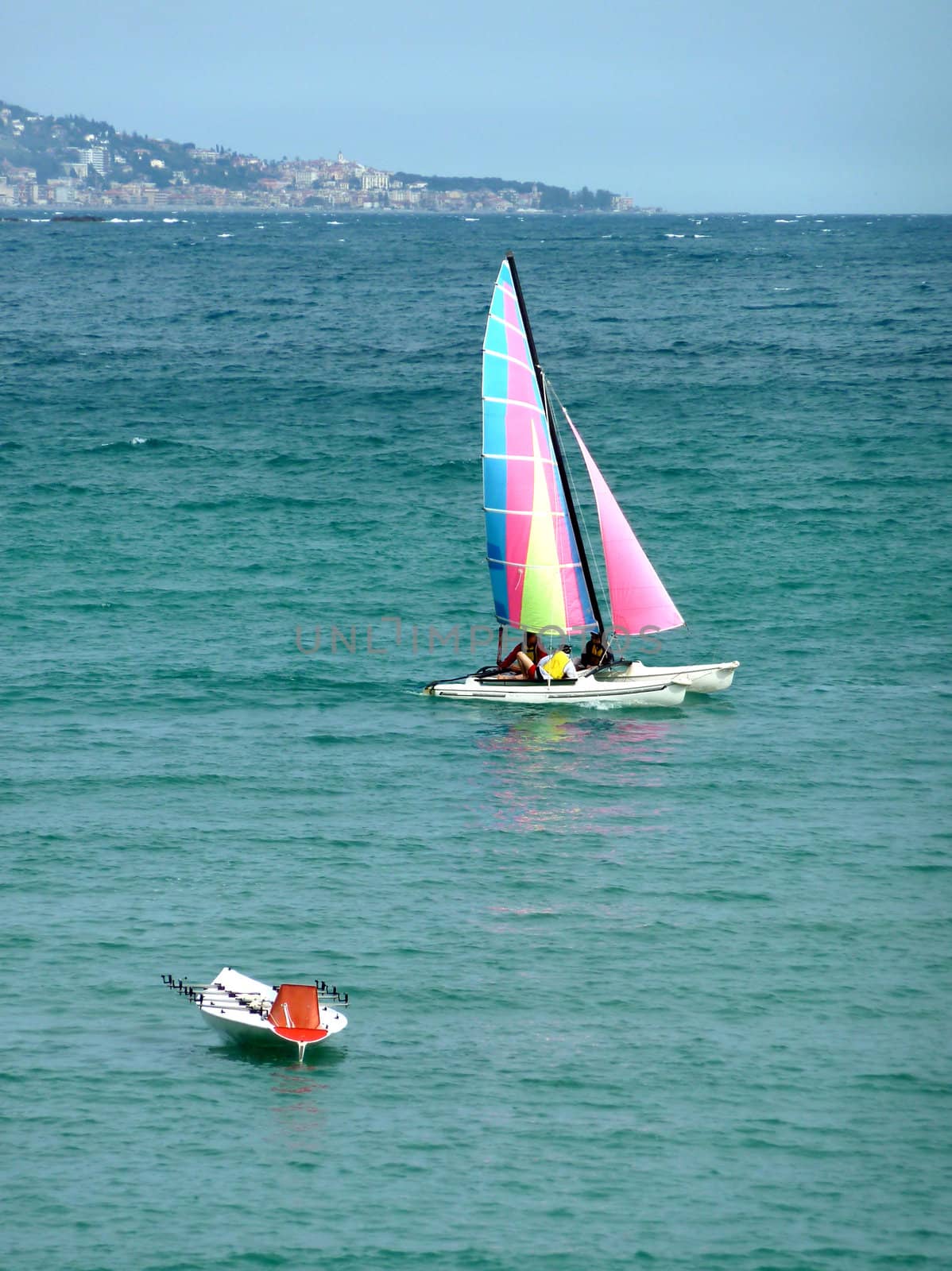 Colorful sailing boat with many people inside and a small white boat floating on the mediterranean sea near the coastline by beautiful weather