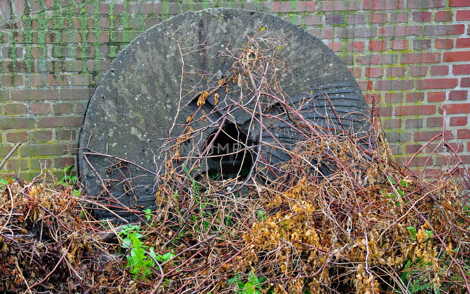 Old broken mill stone at the foot of a closed windmill