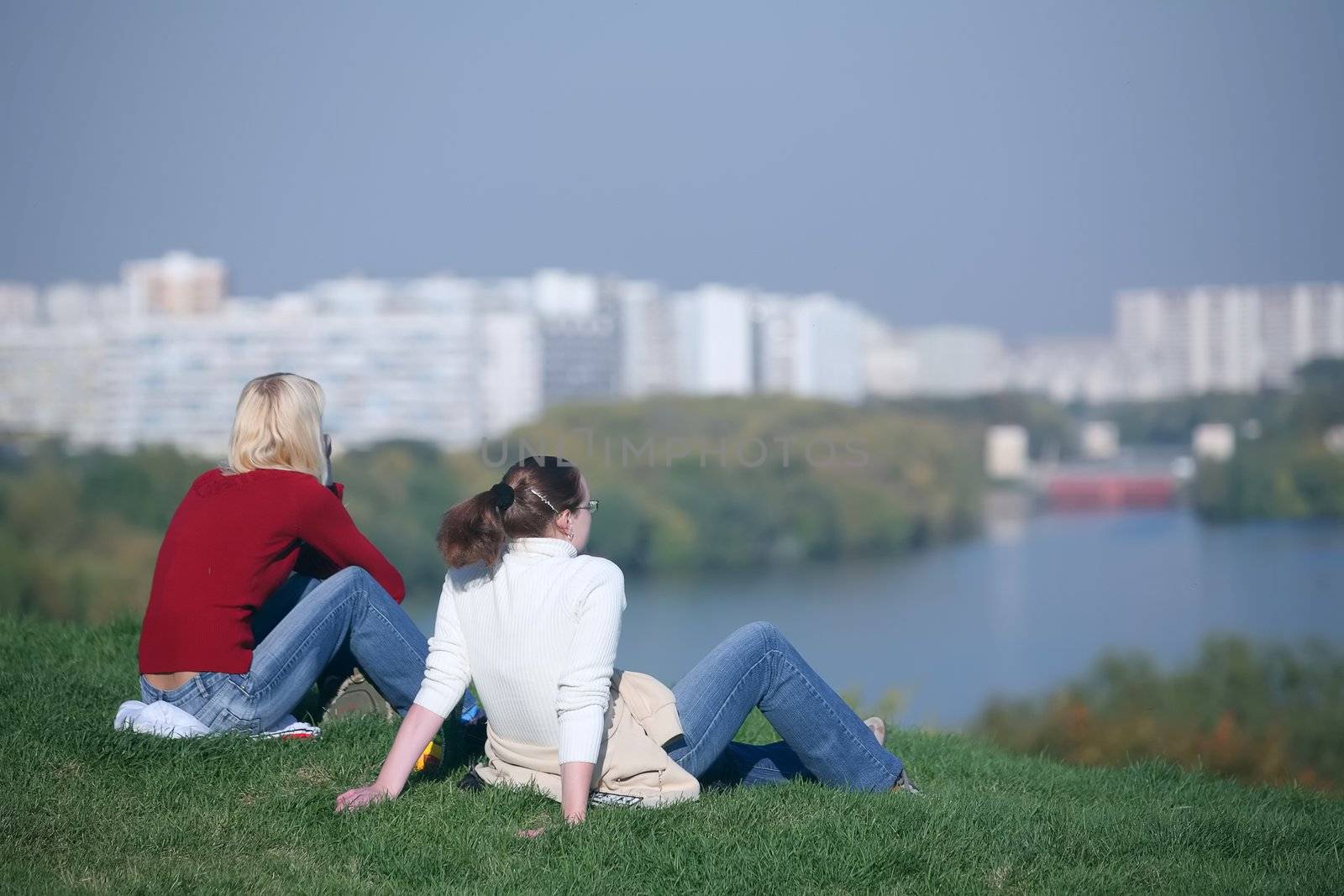 two girls sitting on riverside on background of the city