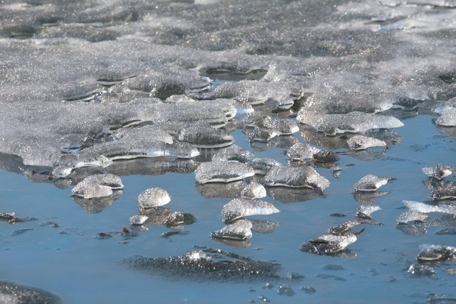 translucent spring ice in blue water on pond