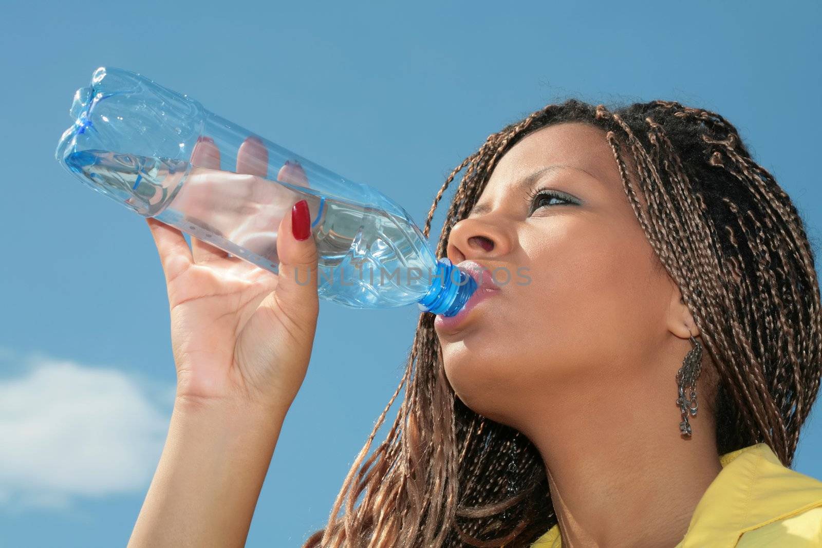 african girl in yellow gown drinking water from blue bottle on sky background