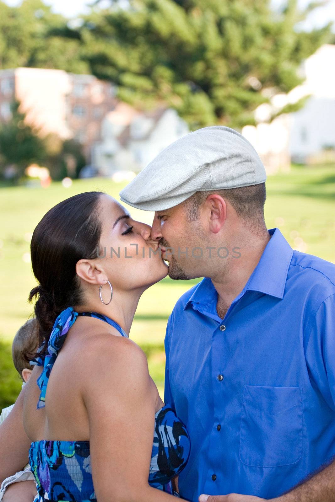 A young couple kissing each other on the lips while the woman holds her baby.