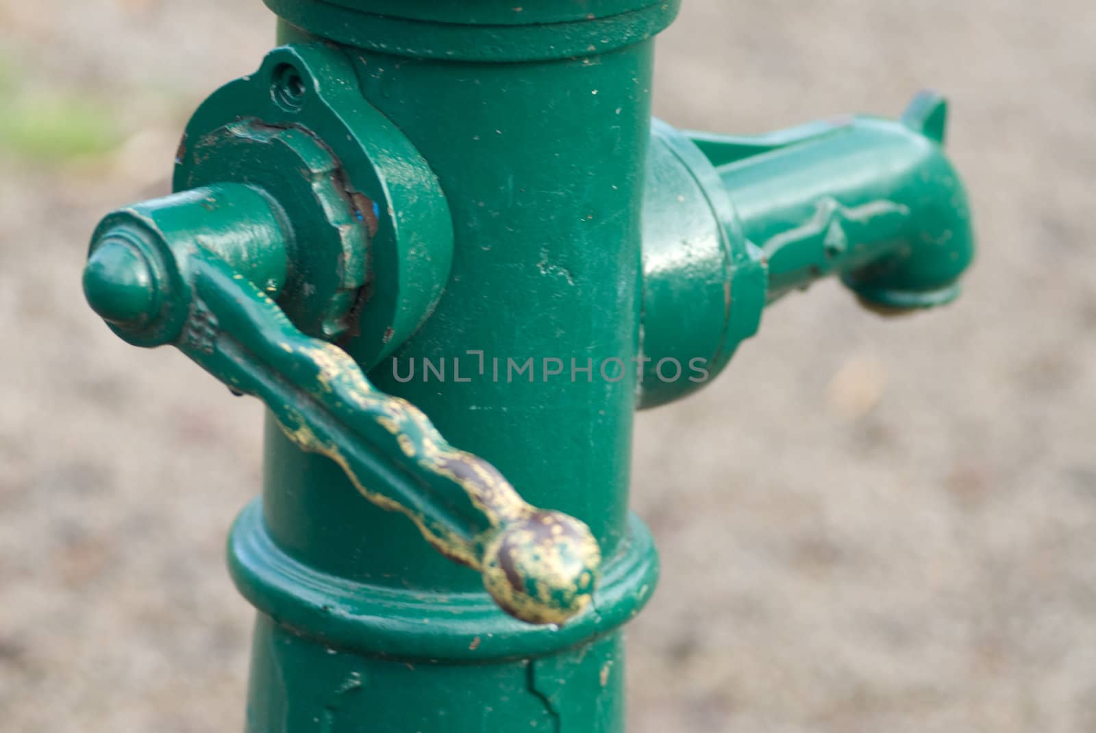 a old green fountain with a grip to pump up the water