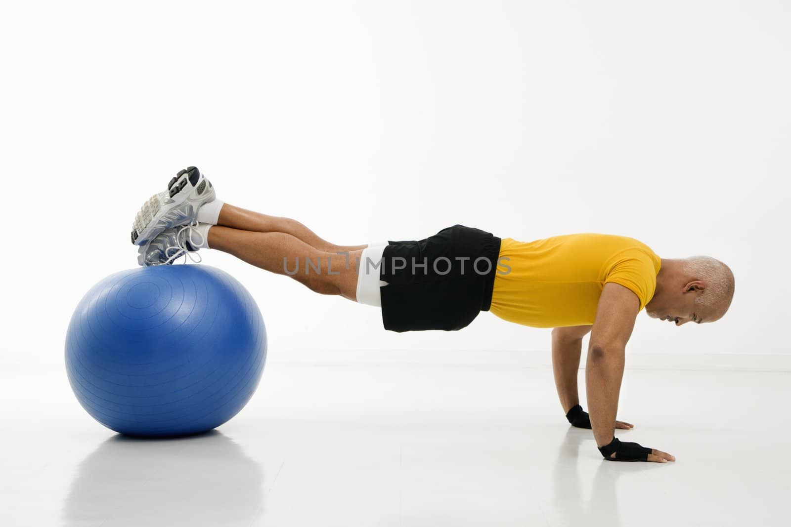 Side view of mid adult multiethnic man doing pushups while balancing on blue exercise ball.