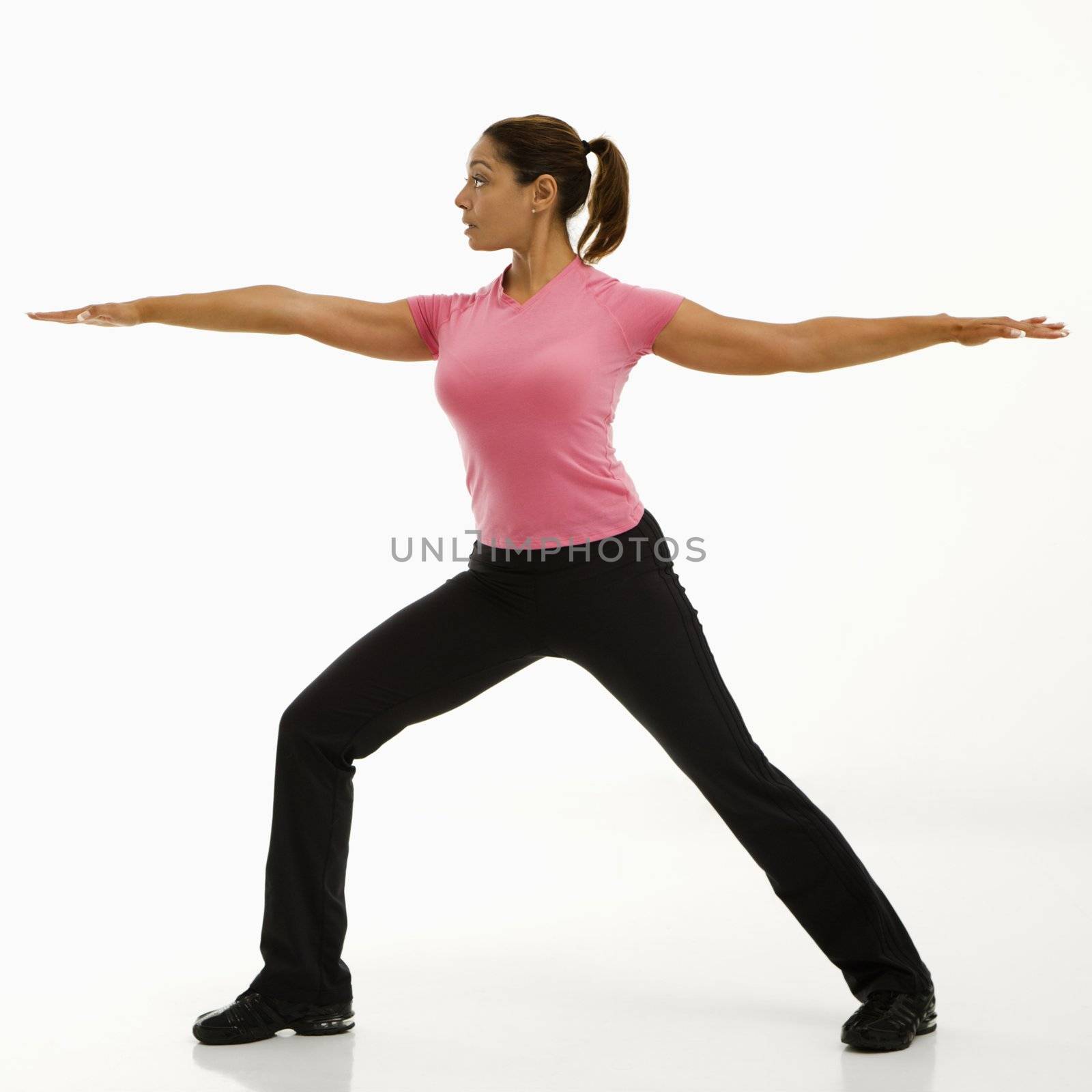 Side view of mid adult multiethnic woman wearing exercise clothing standing in yoga warrior pose.