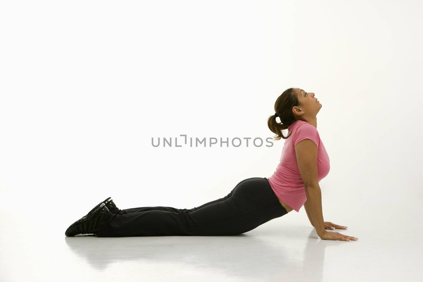 Side view of mid adult multiethnic woman wearing exercise clothing holding cobra yoga pose.