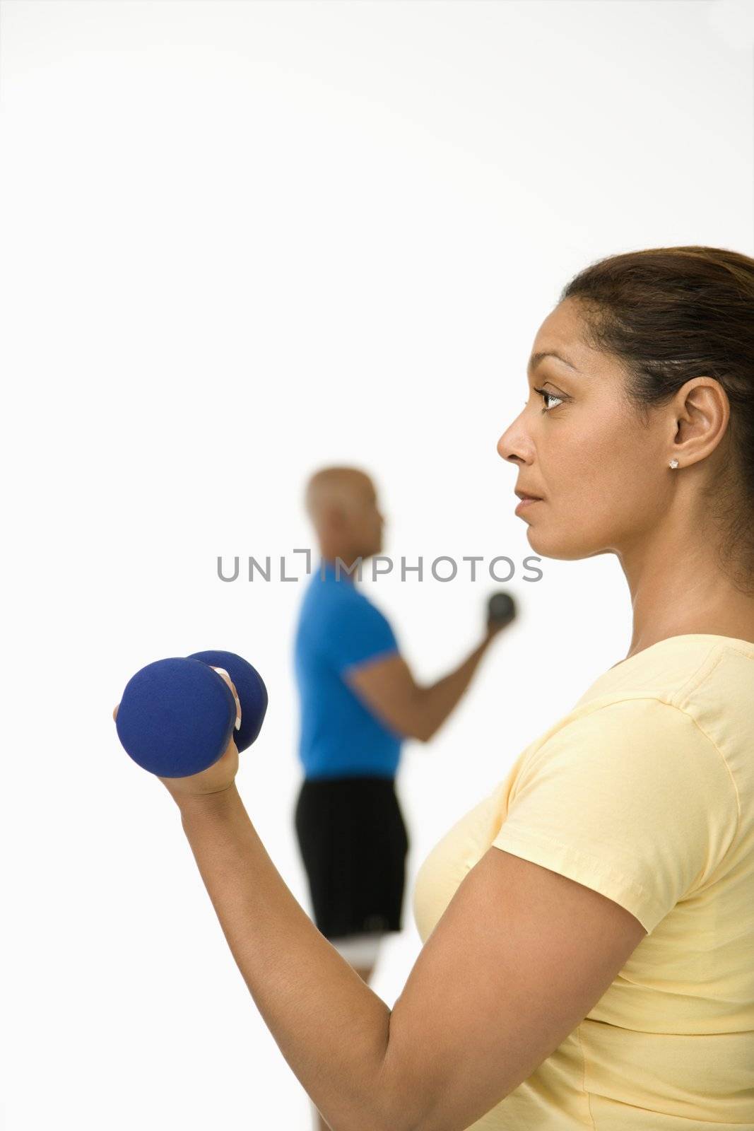 Close up of smiling mid adult multiethnic woman exercising using dumbbells with mid adult multiethnic man in background.