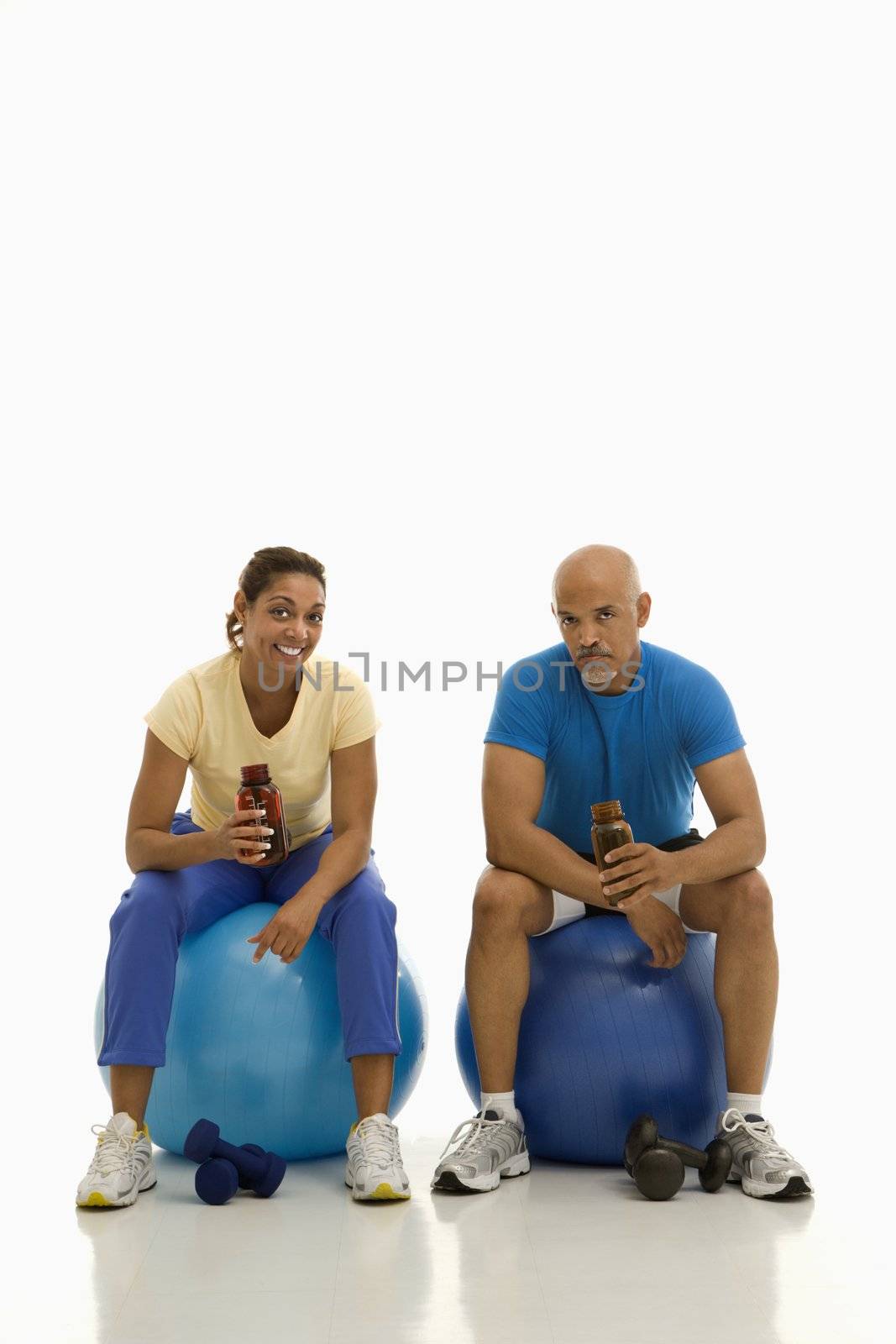 Mid adult multiethnic man and woman sitting on blue exercise balls taking a break.