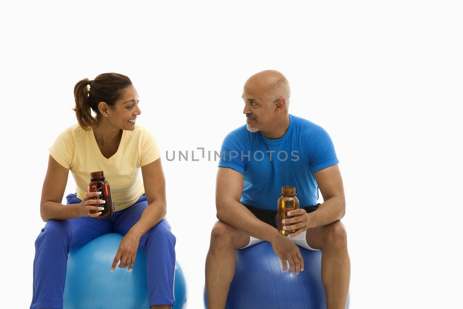 Mid adult multiethnic man and woman sitting on blue exercise balls looking at each other.