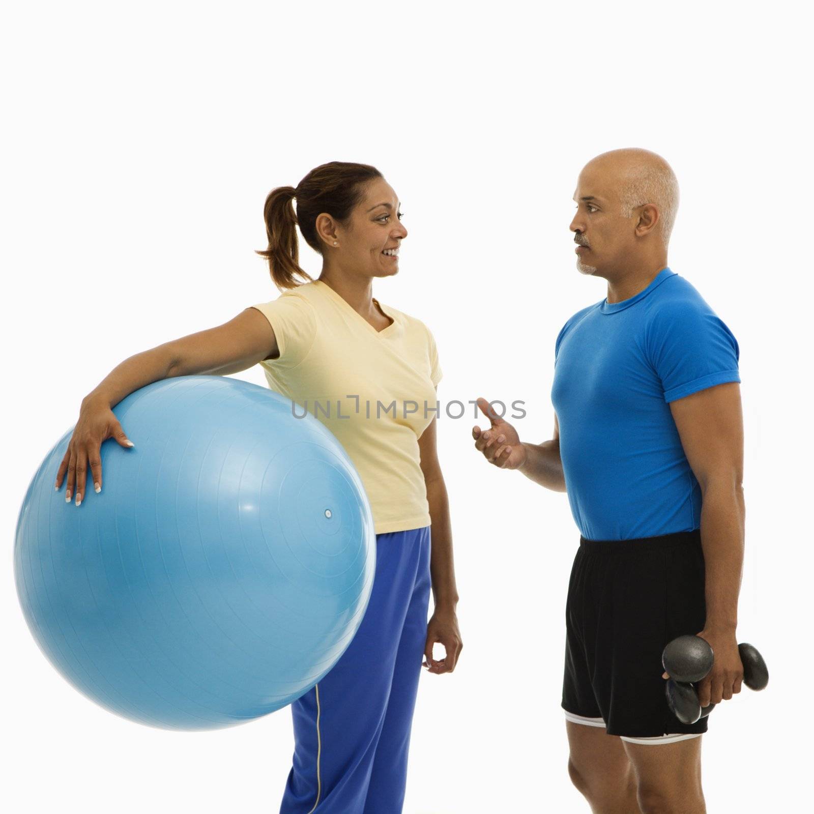 Mid adult multiethnic woman holding blue exercise ball standing with mid adult multiethnic man looking at each talking.