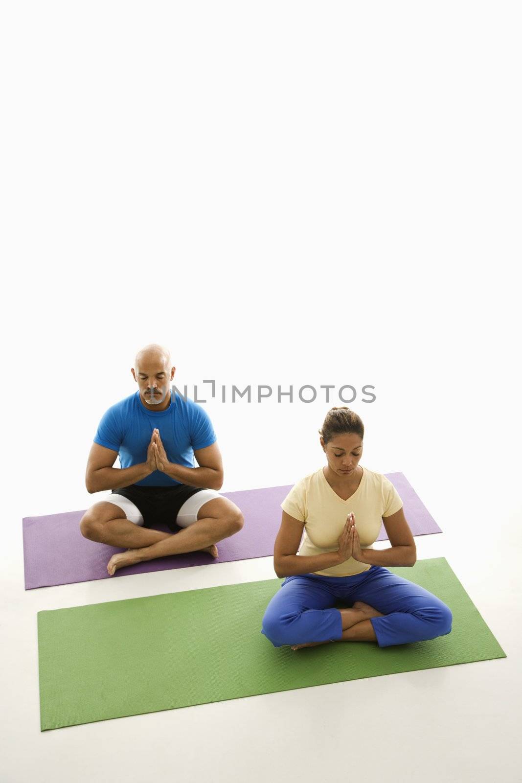 Mid adult multiethnic man and woman sitting in Namaste position on exercise mats with eyes closed and hands at heart center.