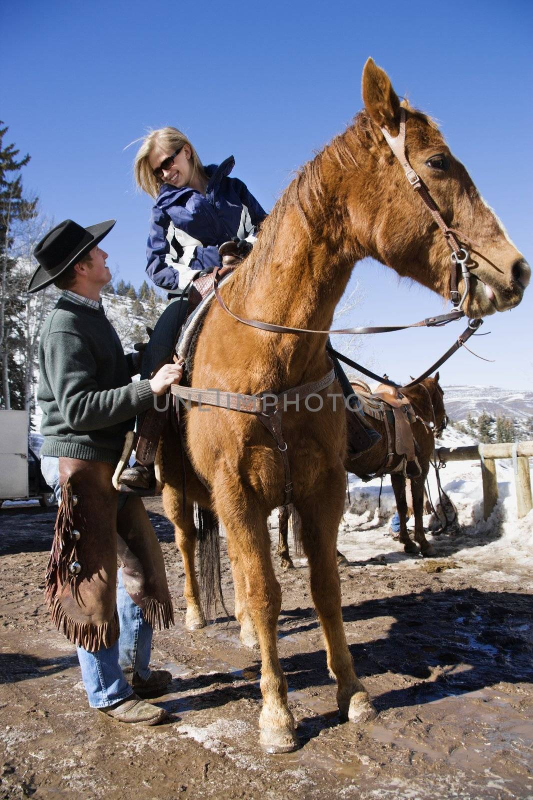 Wrangler talking to young Caucasian woman on horsebaclk.