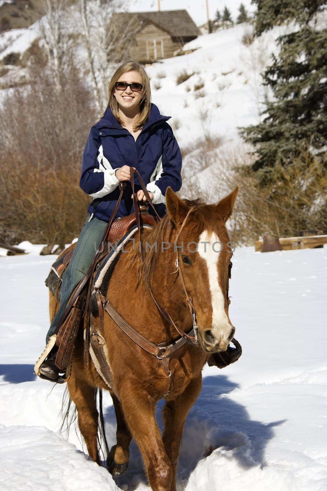 Young Caucasian woman horseback riding in snow and smiling at viewer.